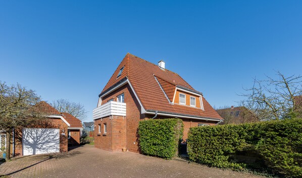 A two-story house with a red-tiled roof, brick walls, and a paved driveway. - Charming Beachside Apartment "Strandkorb" in Büsum - Ideal for Families (Büsum)