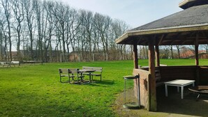 Ein Sitzbereich im Freien mit Tischen und Bänken, ein überdachter Pavillon und eine Rasenfläche.