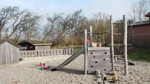 Ein Spielplatz mit Rutsche, Kletterwand und einem hölzernen Spielhäuschen.