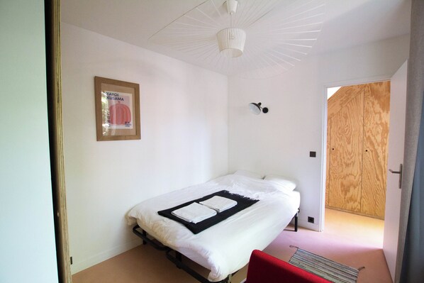 A bedroom with a bed, a framed picture on the wall, a ceiling fan, and a wooden door.