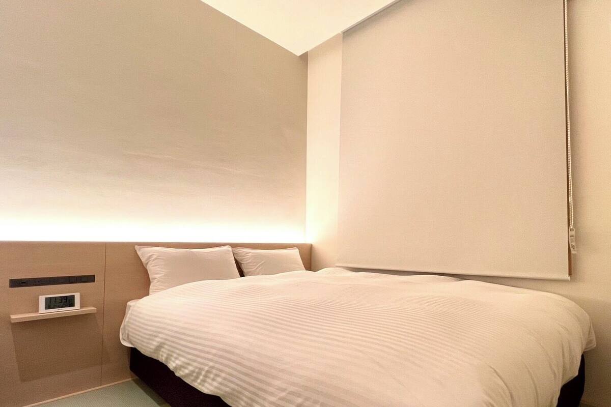 Une chambre d’hôtel moderne avec un grand lit, une table de chevet avec une horloge et une grande fenêtre.