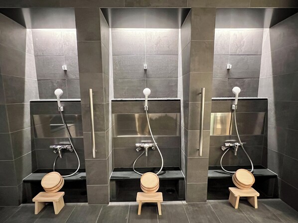 Un baño moderno con tres cabinas de ducha separadas, cada una con un cabezal de ducha manual y un taburete de madera.