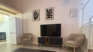A modern living room with a black coffee table, two beige armchairs, a black TV stand, and abstract wall art. - SANTA ANA - SEASONAL RENTAL (Alicante (Alacant))