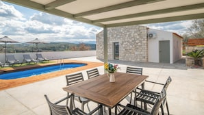 A covered outdoor area with a pool, lounge chairs, and a dining table. - Villa Lakioto (Polemarchi)
