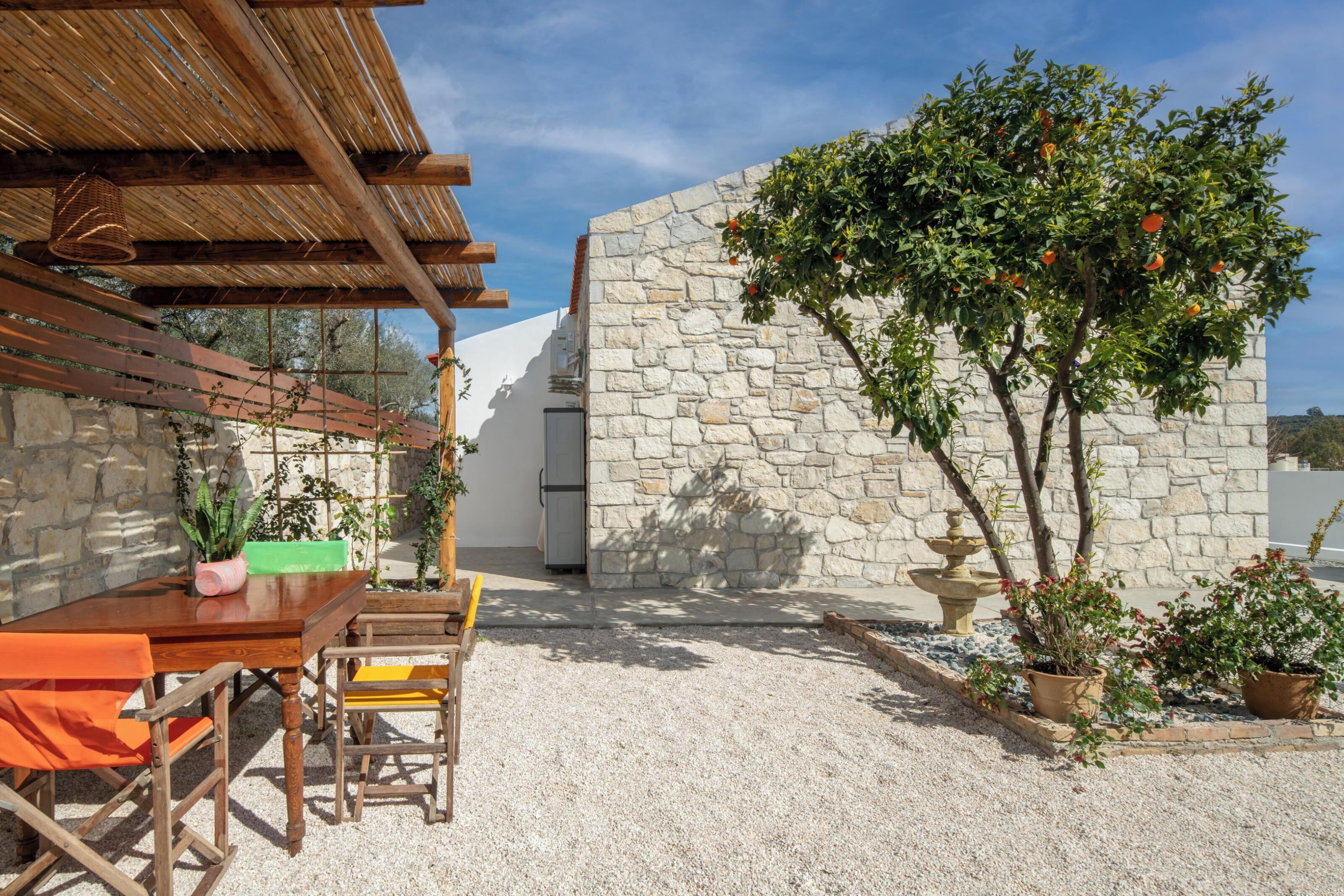 A patio with a wooden table and chairs, surrounded by stone walls and potted plants.