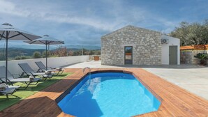 A rooftop pool with lounge chairs and umbrellas, a stone building, and a view of the landscape. - Villa Lakioto (Polemarchi)
