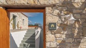 A stone building with a wooden door frame and a staircase leading to a covered outdoor area. - Villa Lakioto (Polemarchi)