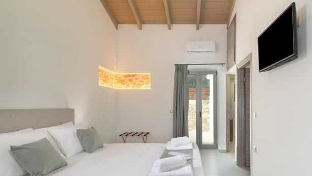 A hotel room with a bed, a TV, a wall-mounted air conditioner, and a view through a glass door. - Villa Lakioto (Polemarchi)