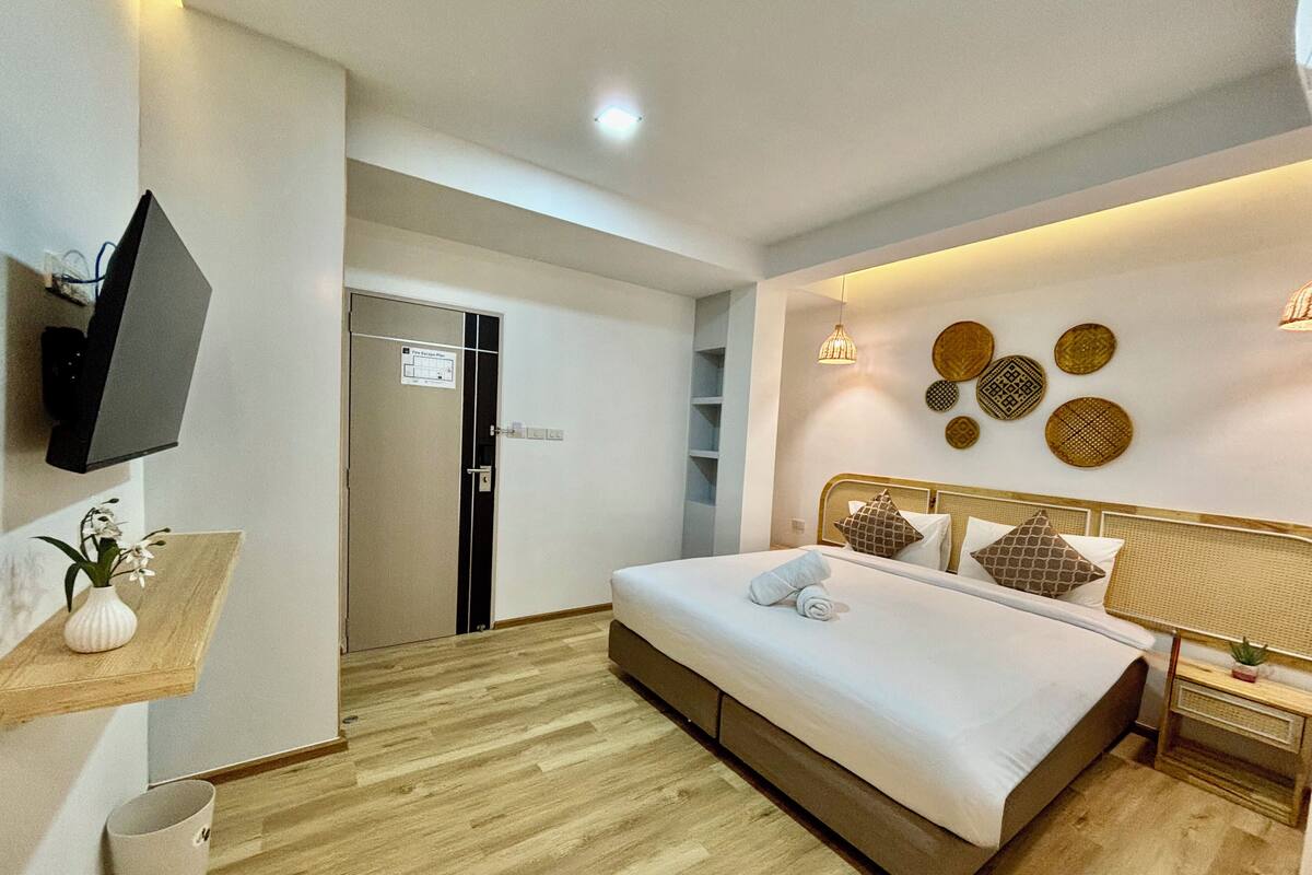 Una habitación de hotel moderna con una cama grande, un televisor montado en la pared, una planta pequeña en un estante y una puerta con un letrero.