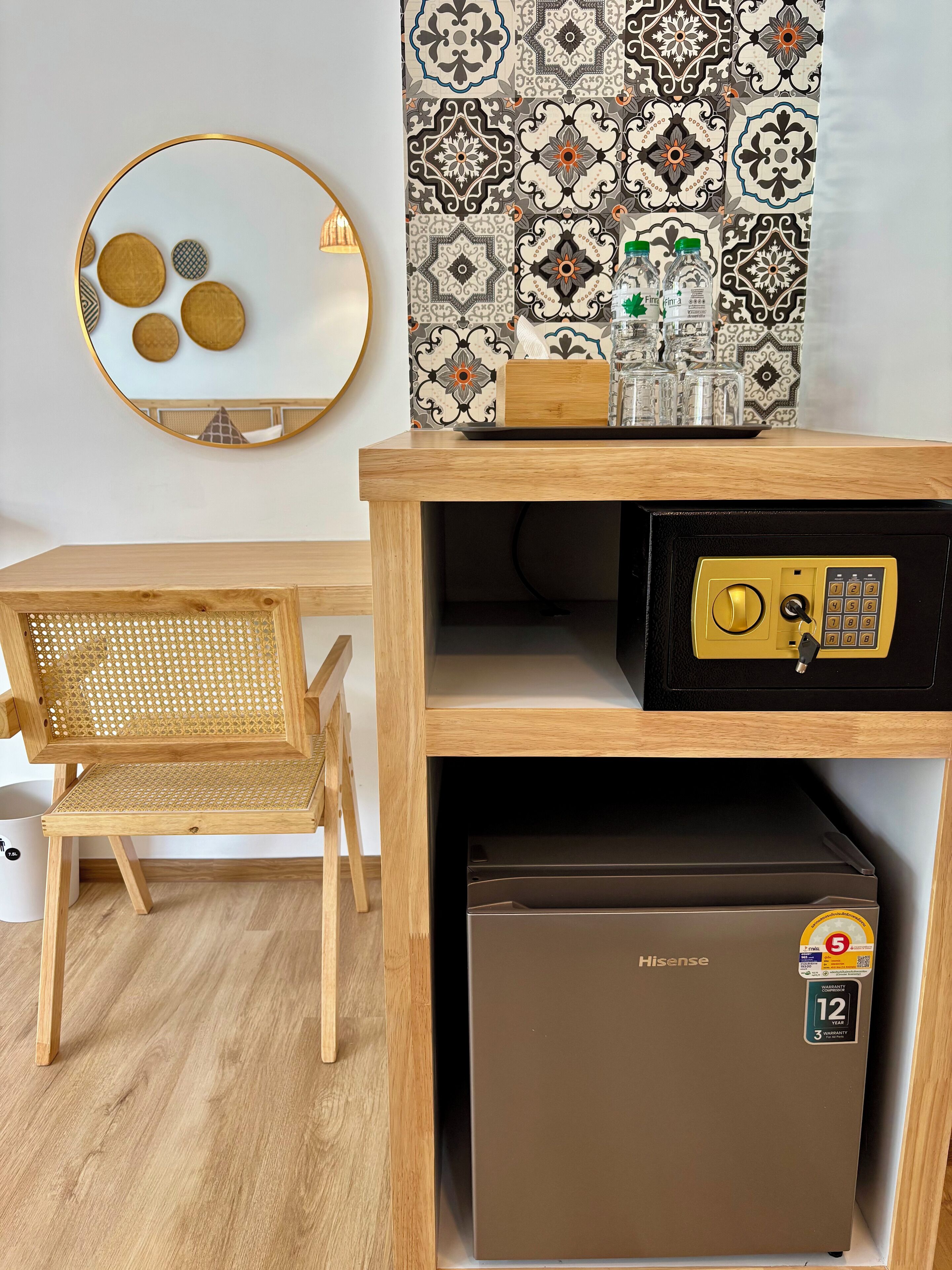 Une pièce de taille modeste, comprenant un bureau en bois, une chaise, un petit réfrigérateur et un coffre-fort fixé au mur.