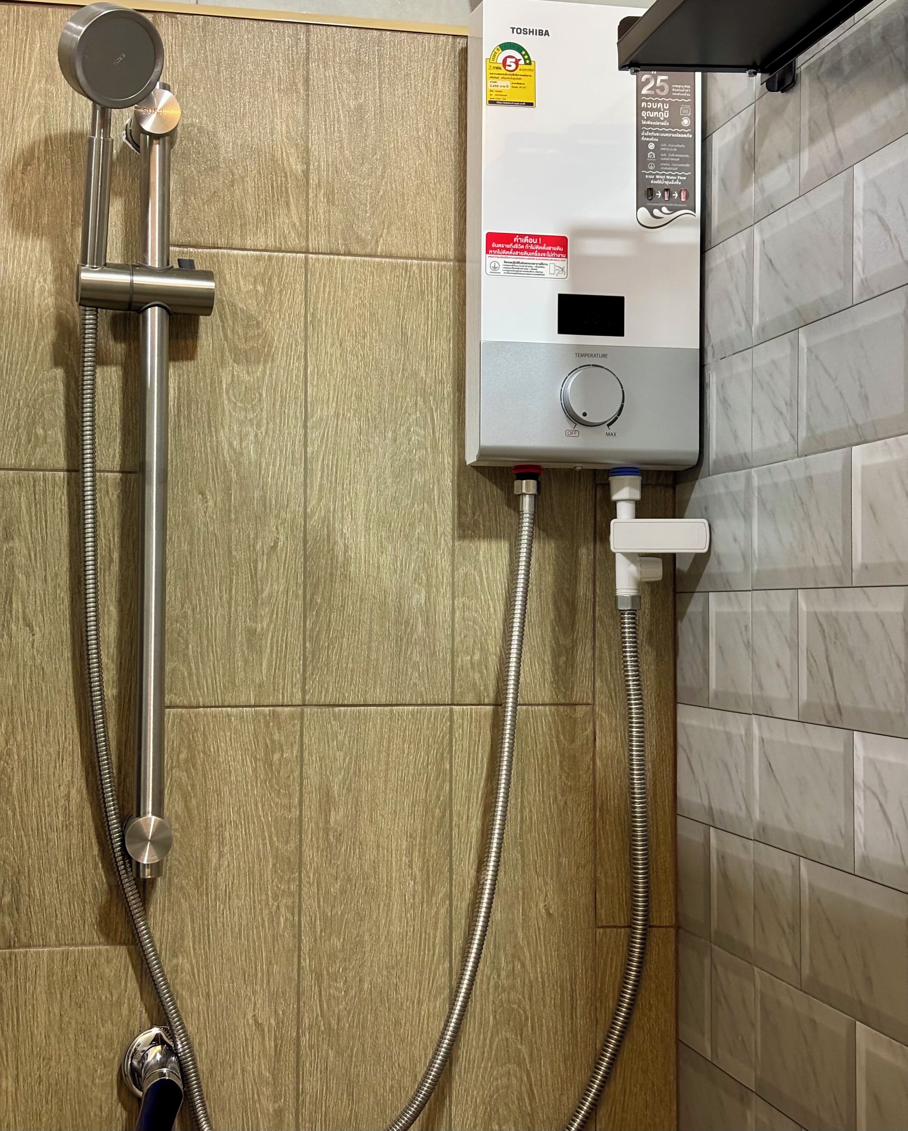 Ein an der Wand montierter Durchlauferhitzer mit Bedienfeld, einem flexiblen Duschschlauch und einem Wandarmaturen-Set.