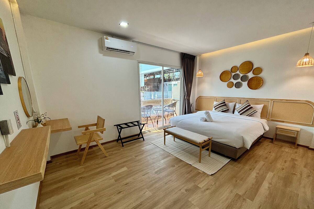 Una habitación de hotel moderna con una cama grande, un escritorio pequeño, una silla y un balcón con mobiliario exterior.