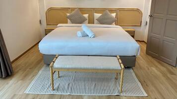 A neatly made bed with a white comforter and two pillows, a wooden bench at the foot of the bed, a woven headboard, and a wall with circular woven wall hangings.