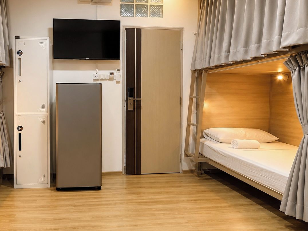A compact room with a bunk bed, a refrigerator, a television, and a wardrobe.