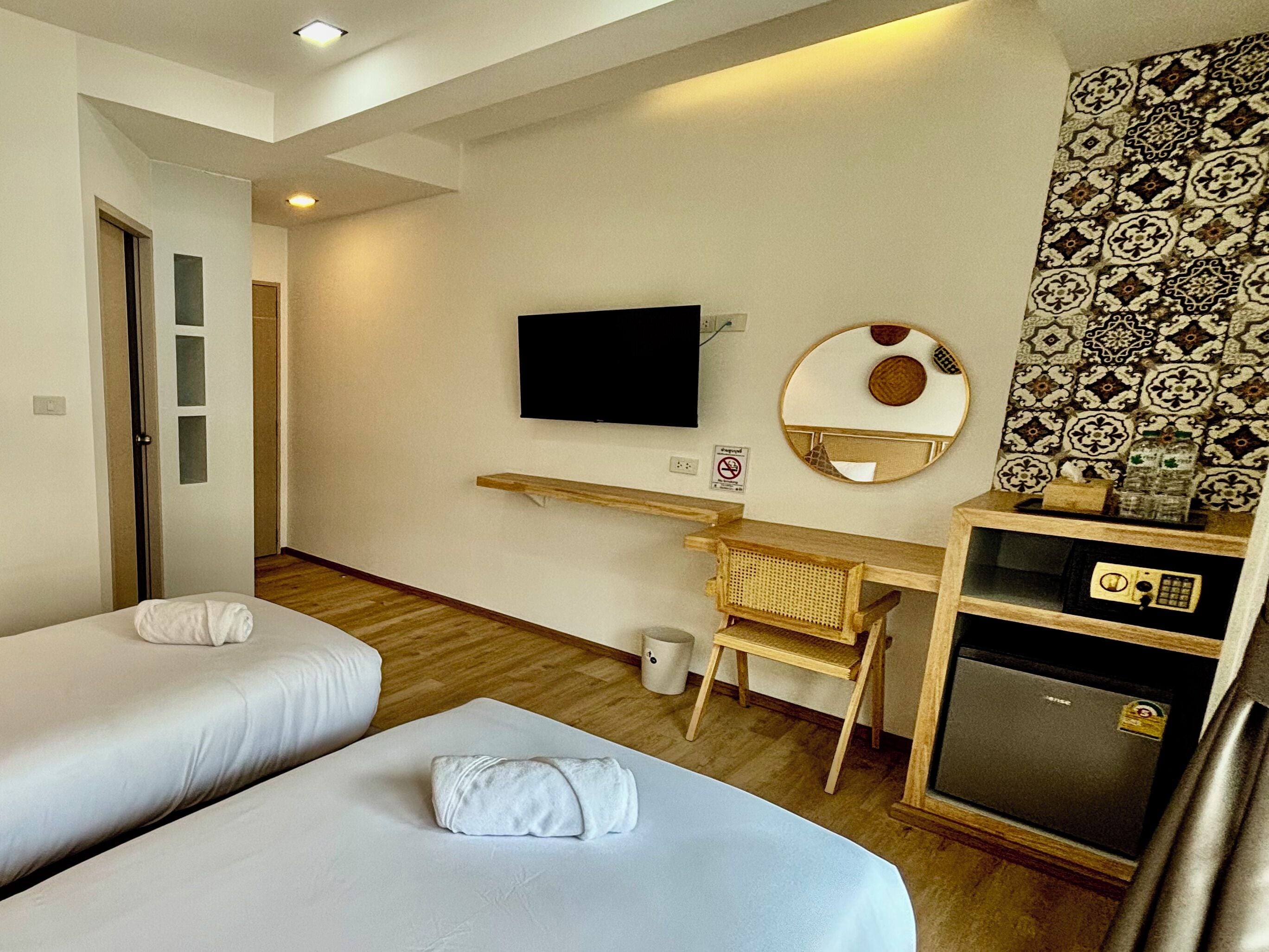 A hotel room with two beds, a TV, a small desk, a mirror, and a minibar.