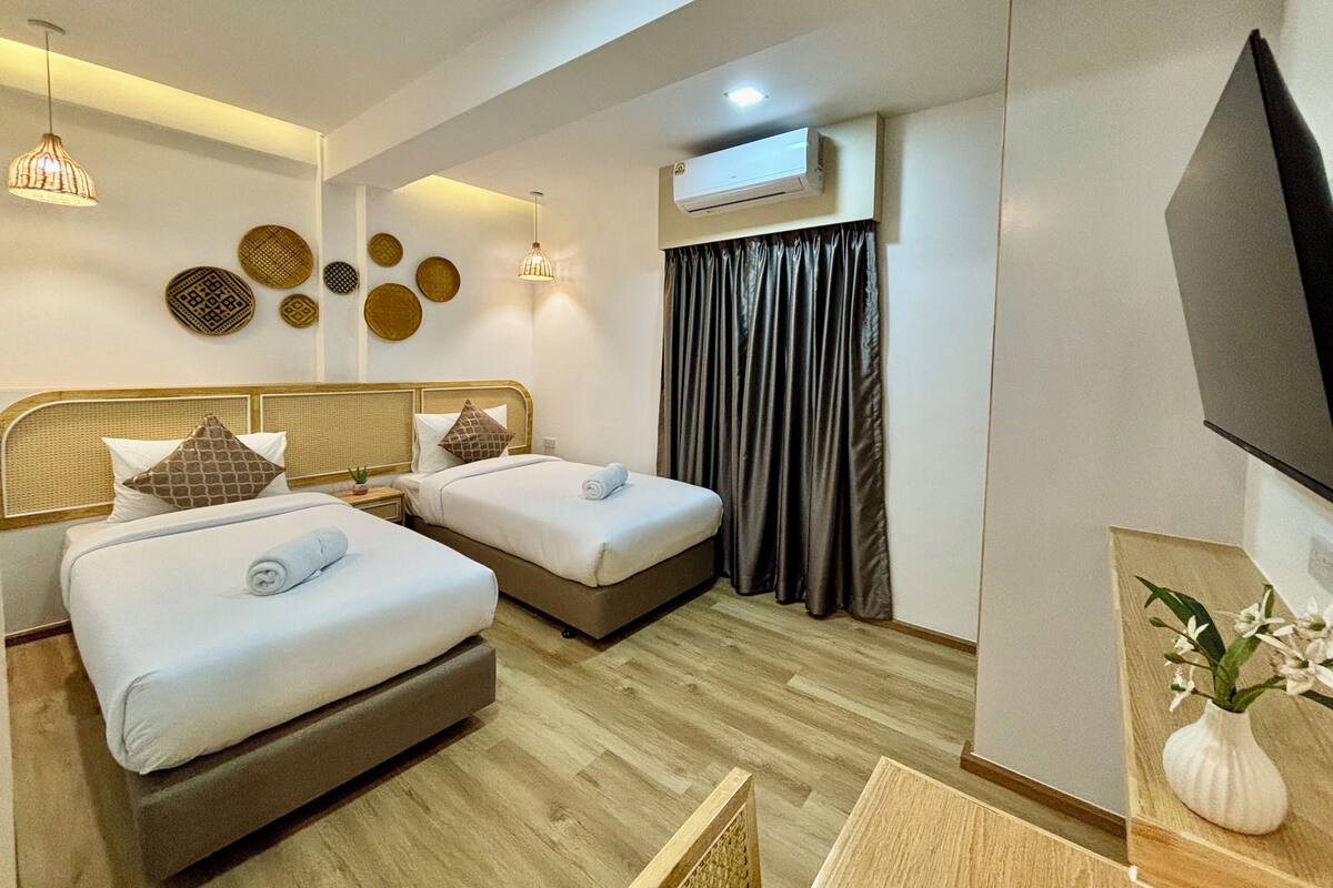 Habitación de hotel con dos camas, un televisor de pantalla plana, un equipo de aire acondicionado y una pared decorativa con cestas tejidas.