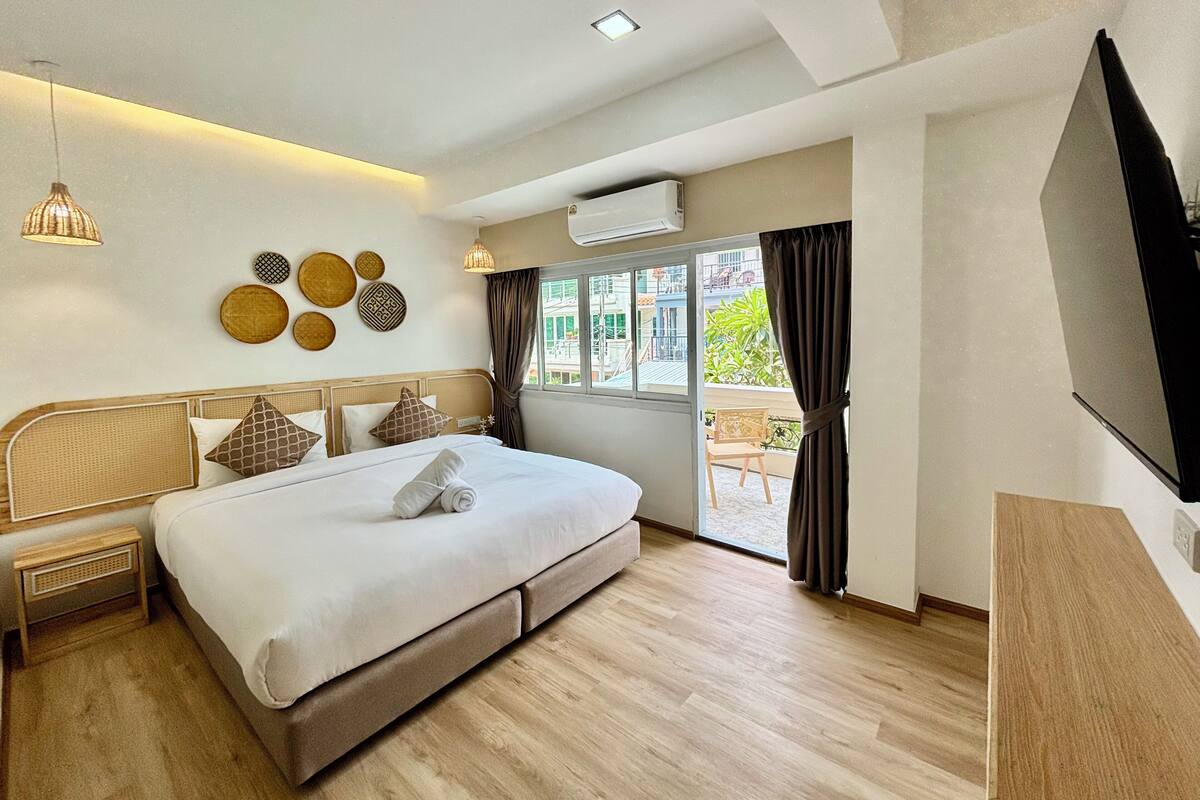Una habitación de hotel moderna con una cama grande, televisión y balcón con cortinas.