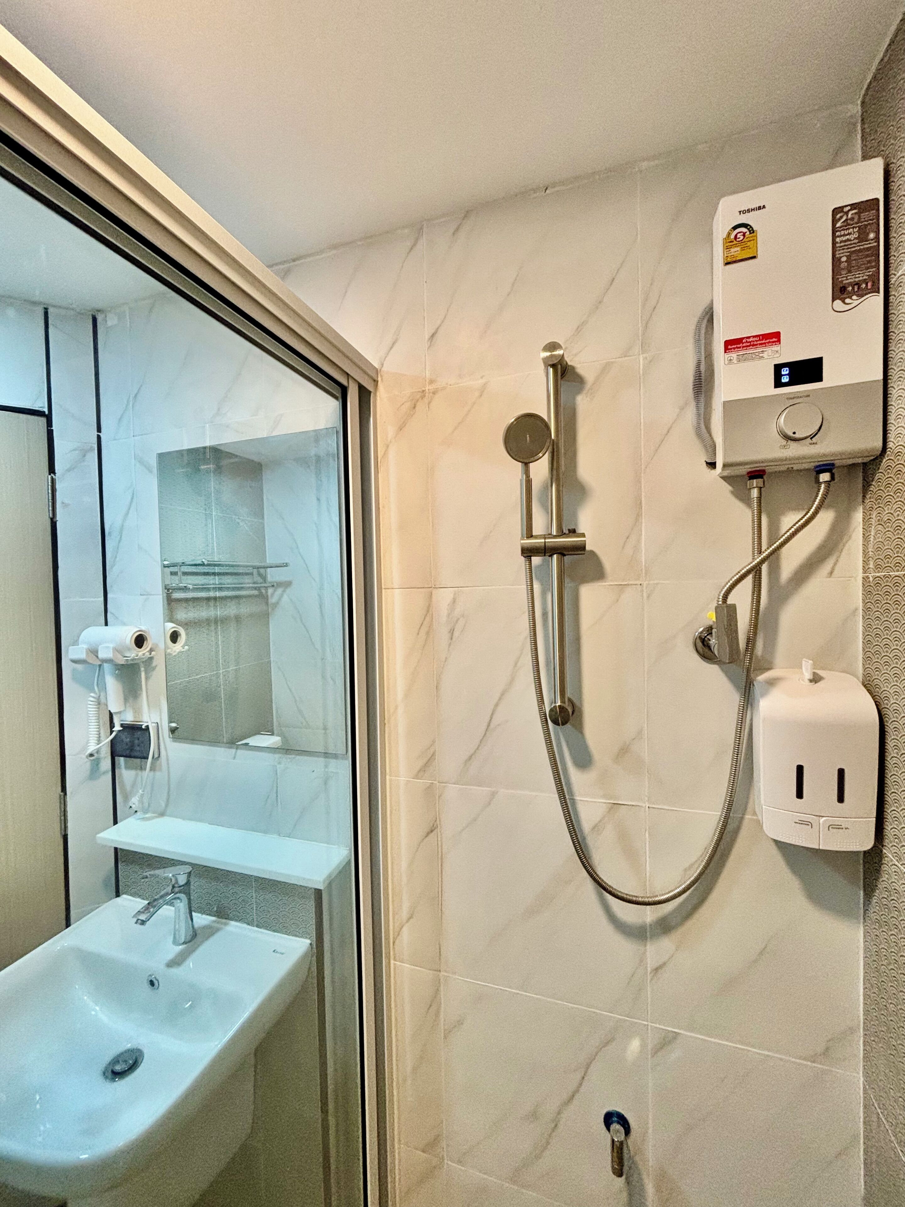 A bathroom with a glass shower enclosure, a white sink, and a wall-mounted toilet paper dispenser.