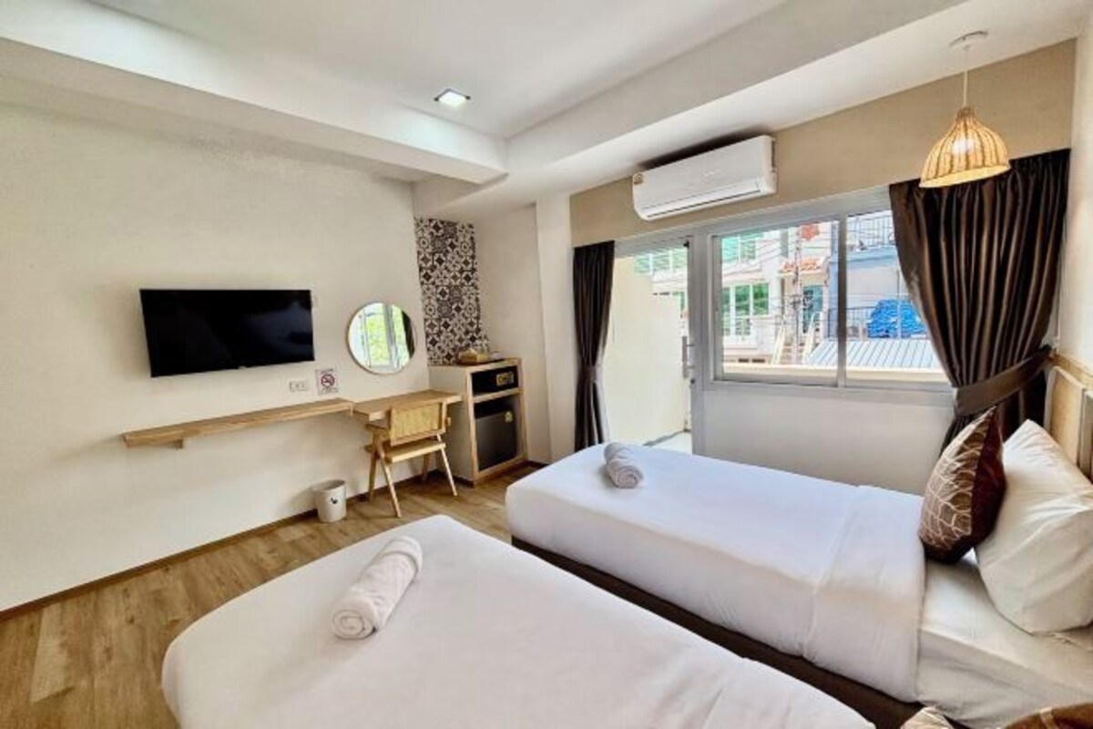 Habitación de hotel con dos camas, un escritorio, un televisor y una ventana con cortinas.