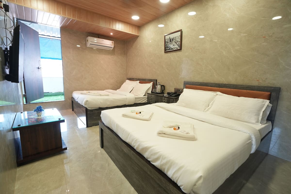 A hotel room with two beds, a wooden ceiling, an air conditioning unit, a framed picture on the wall, and a small table with a decorative item.