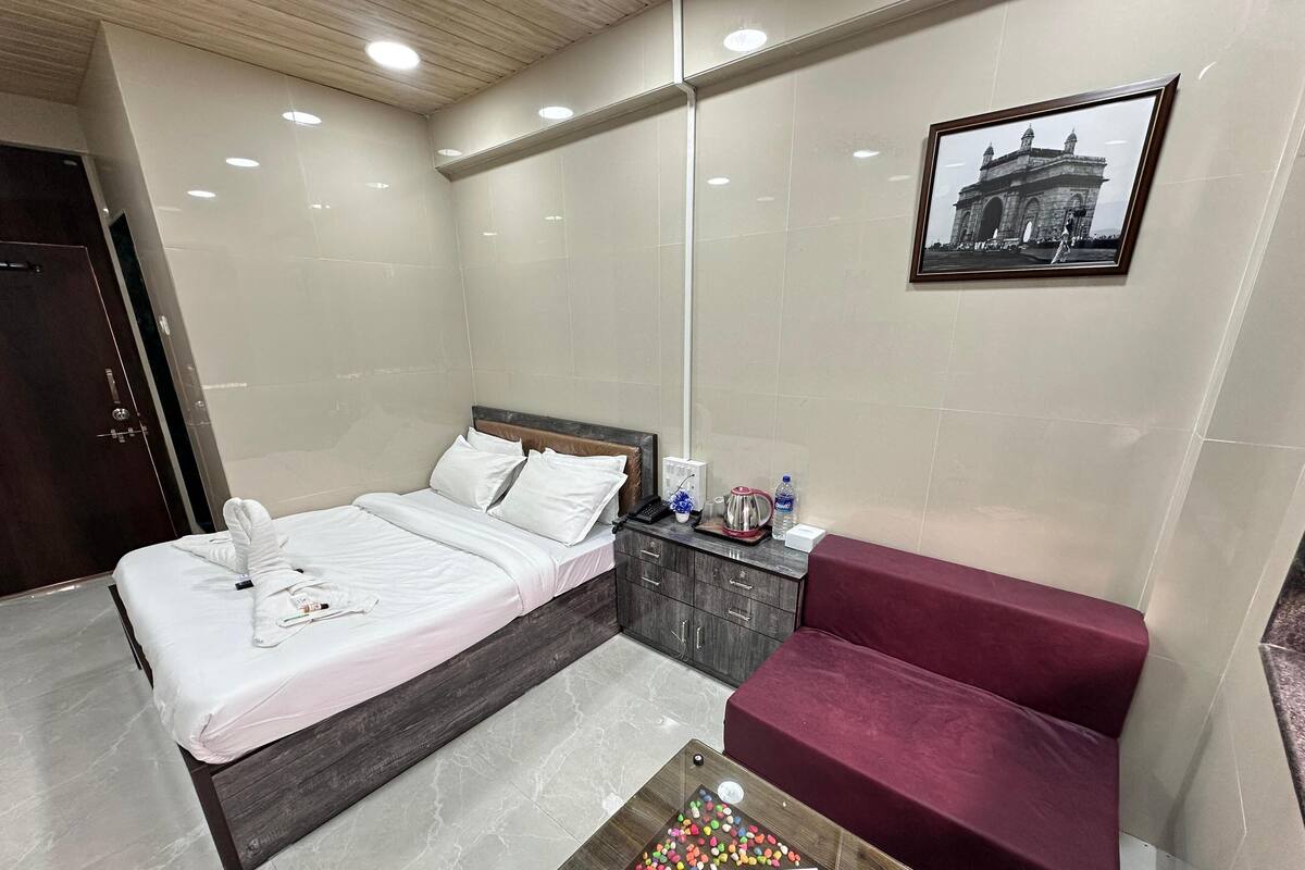 A hotel room with a bed, a bedside table with a kettle, a water bottle, and a framed picture on the wall.