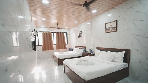 A hotel room with two beds, marble walls, wooden ceiling, and a ceiling fan.