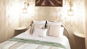 A bedroom with a bed, two bedside tables, a painting on the wall, and two wall-mounted lamps.