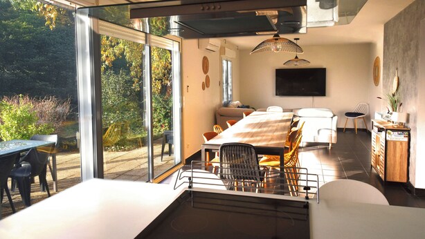 A modern dining area with a glass door leading to a garden, a dining table with chairs, a sofa, a TV, and a small cabinet.