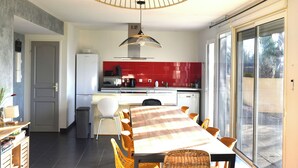 A modern kitchen with a dining area, featuring a large table, chairs, and a hanging light fixture.