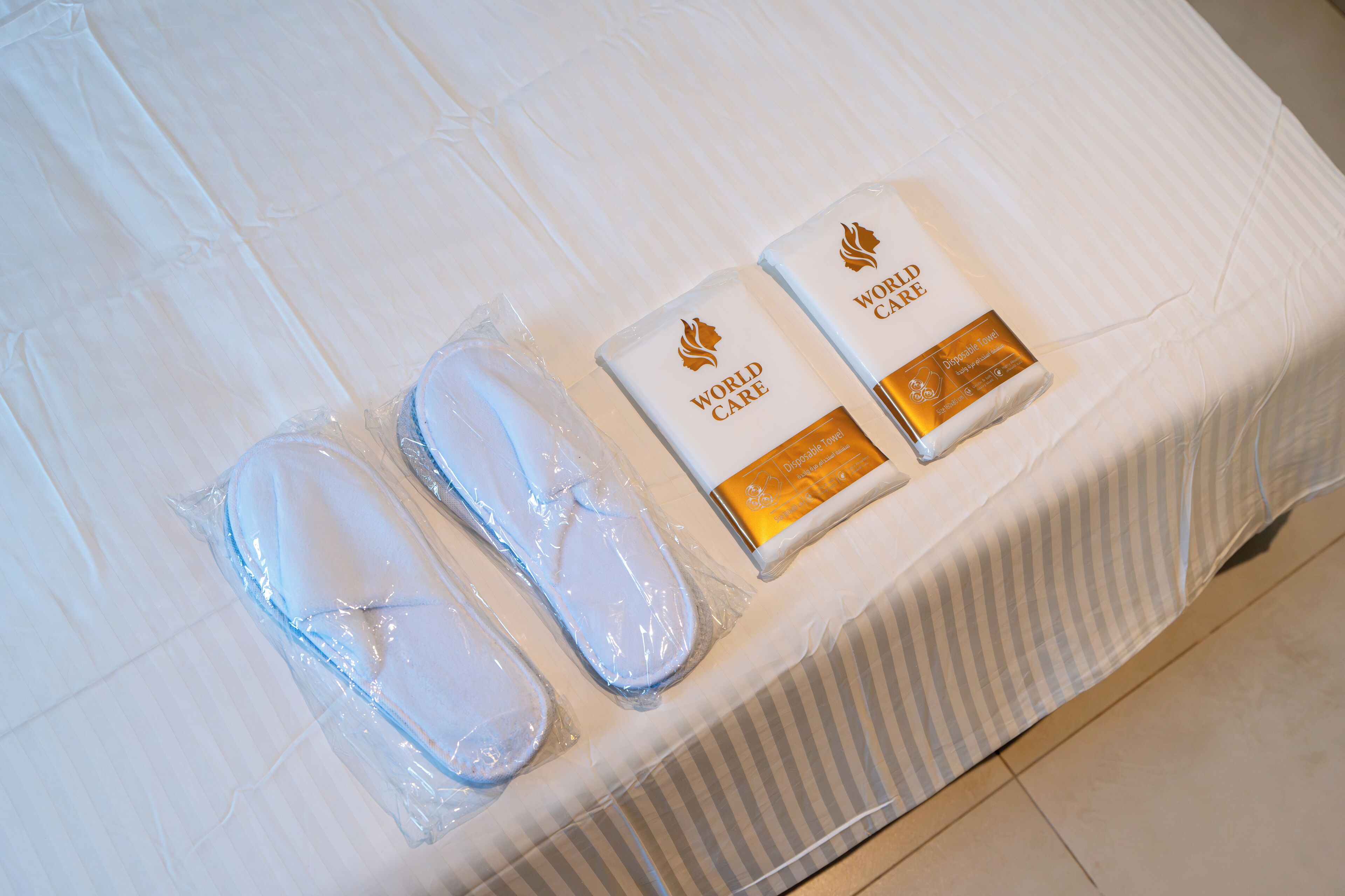 Een net opgemaakt bed met een witte spreidek en twee kussens in plastic verpakt.