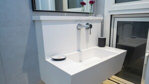 Un baño moderno con un lavamanos blanco, un espejo encima y una ventana a la derecha.