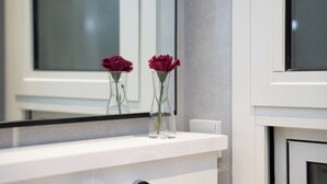 Un tocador de baño con espejo y dos jarrones transparentes con flores rojas.