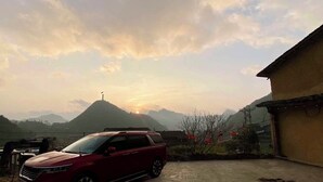 Un SUV rojo estacionado en un patio con montañas al fondo y un edificio a la derecha.