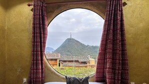 Una habitación con una cama, un ventanal con cortinas y vistas a una montaña y edificios.