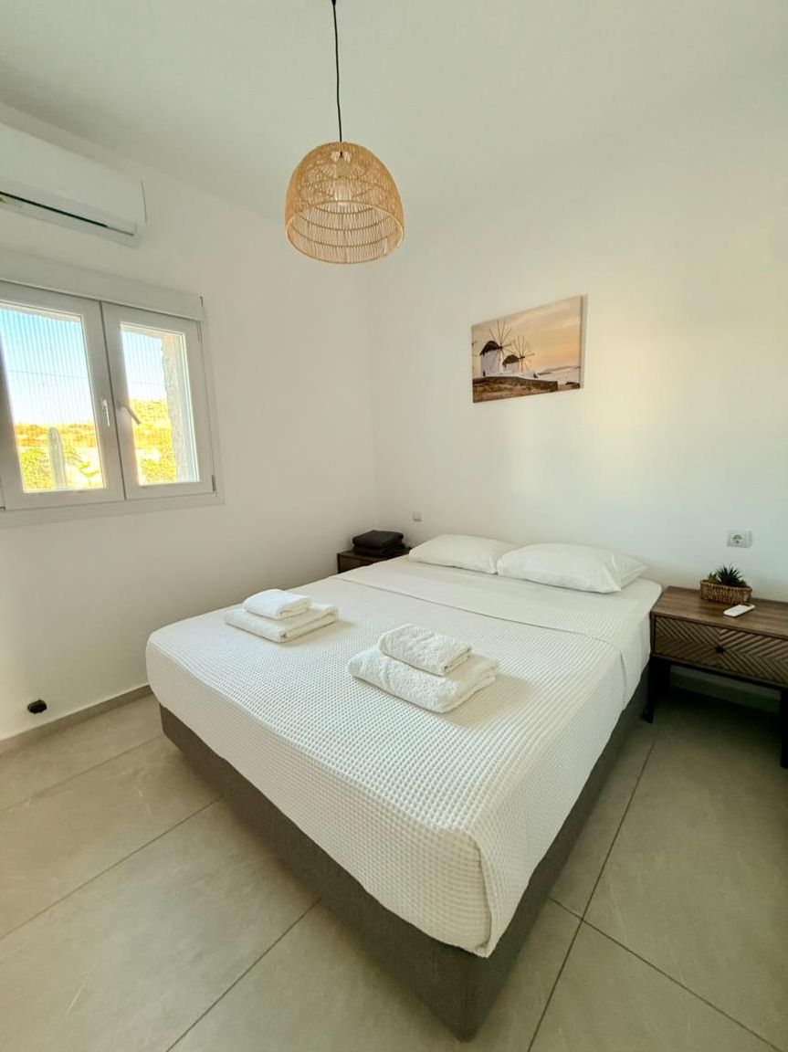Ein Schlafzimmer mit Bett, Nachttischen, einer Hängelampe, einem Fenster und einem Wandbild.