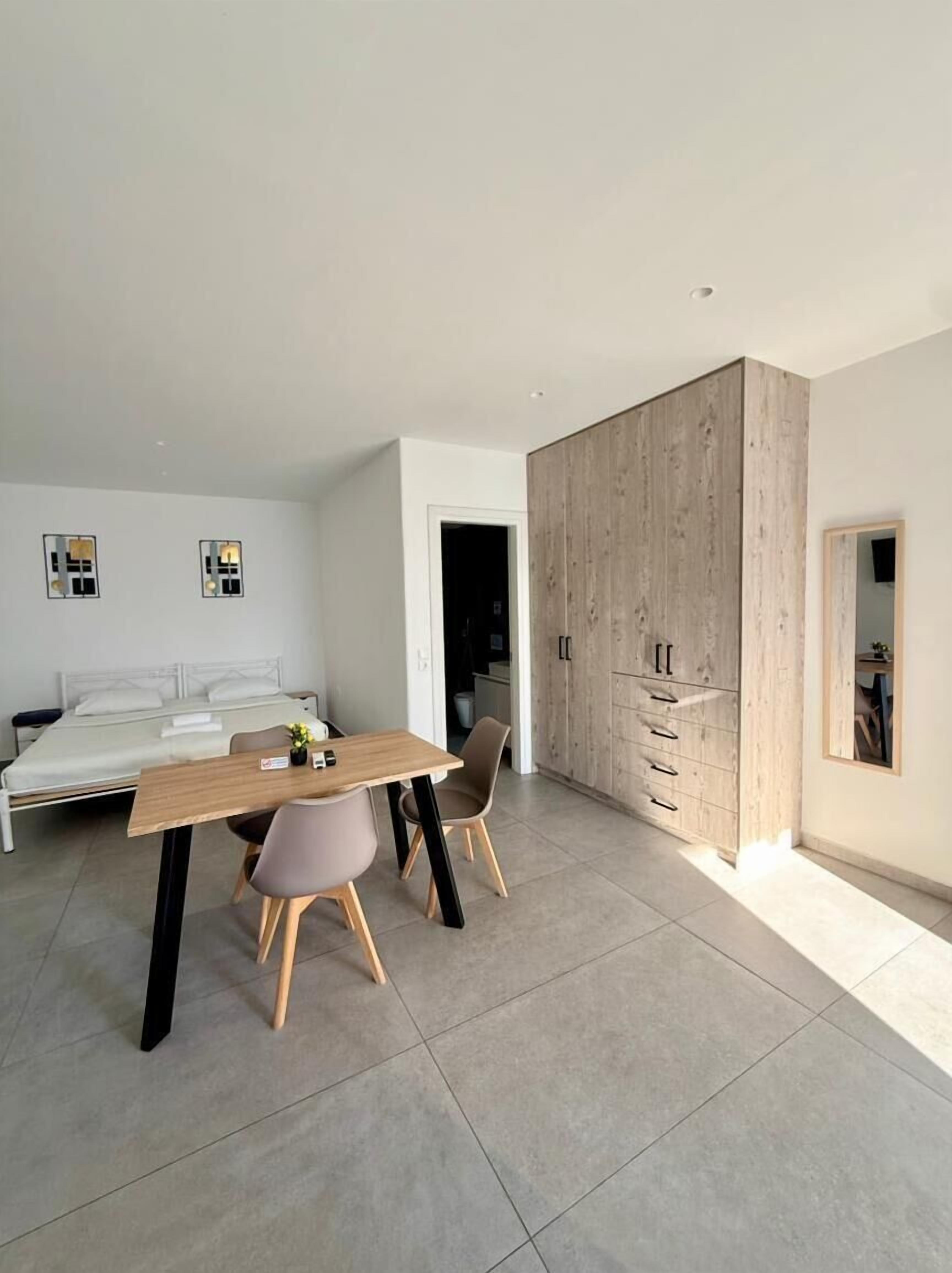 A modern bedroom with a bed, a wooden wardrobe, a dining table with chairs, and a small table with a plant.