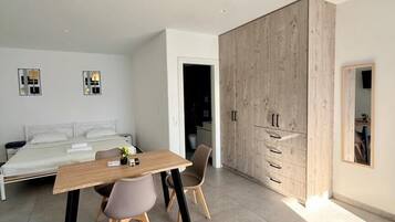 A modern bedroom with a bed, a wooden wardrobe, a dining table with chairs, and a small table with a plant.