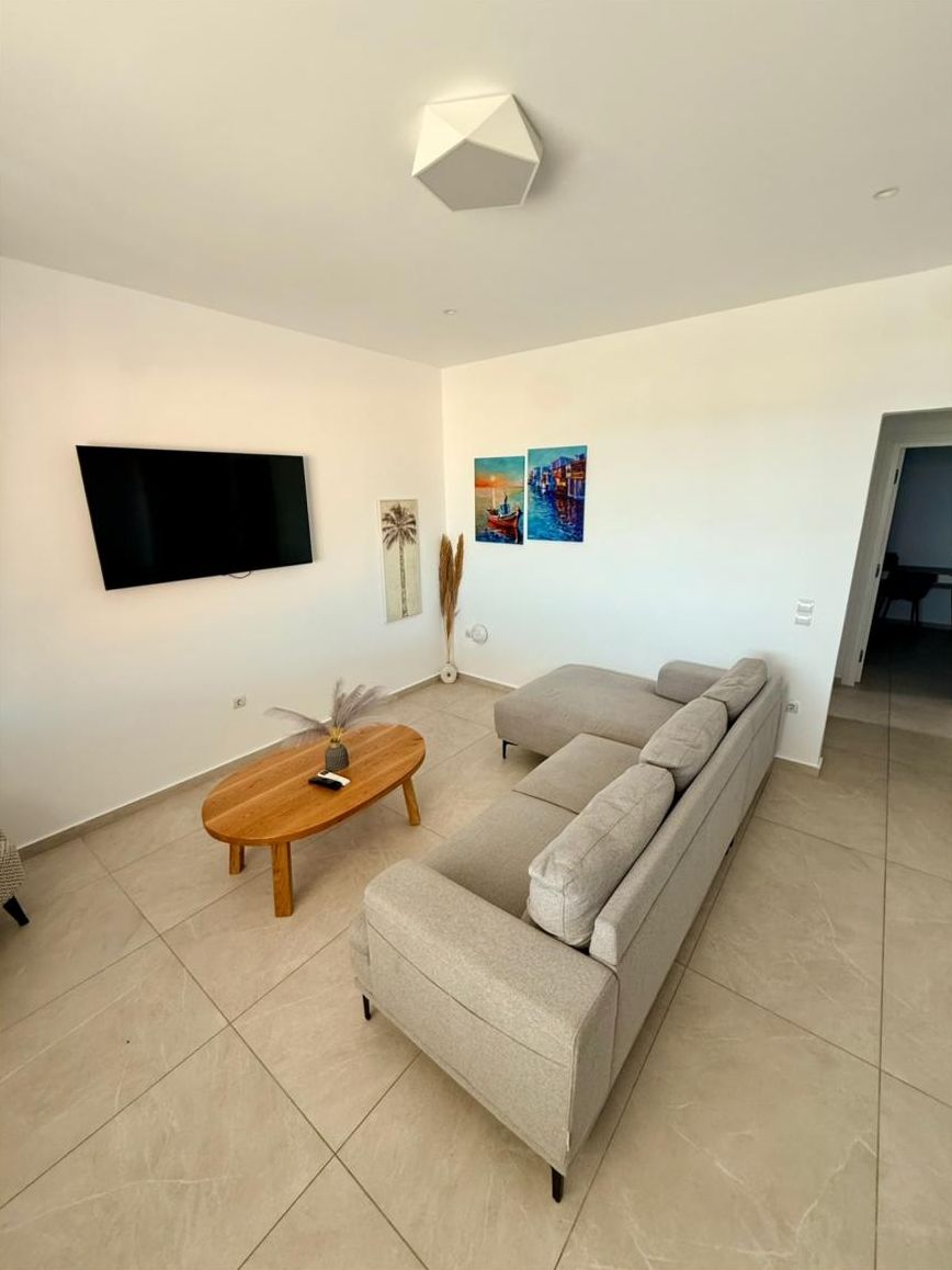 Uma sala de estar moderna com televisão de tela plana, sofá, mesa de centro de madeira e obras de arte nas paredes.