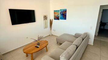 Uma sala de estar moderna com televisão de tela plana, sofá, mesa de centro de madeira e obras de arte nas paredes.