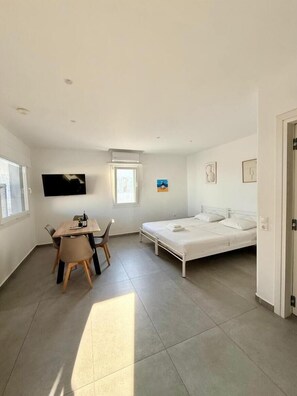 A small, bright room with a bed, a table, and chairs.