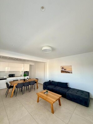 A modern living space with a dining area, a sofa, and a kitchen in the background. - Psaros Village (Mykonos)