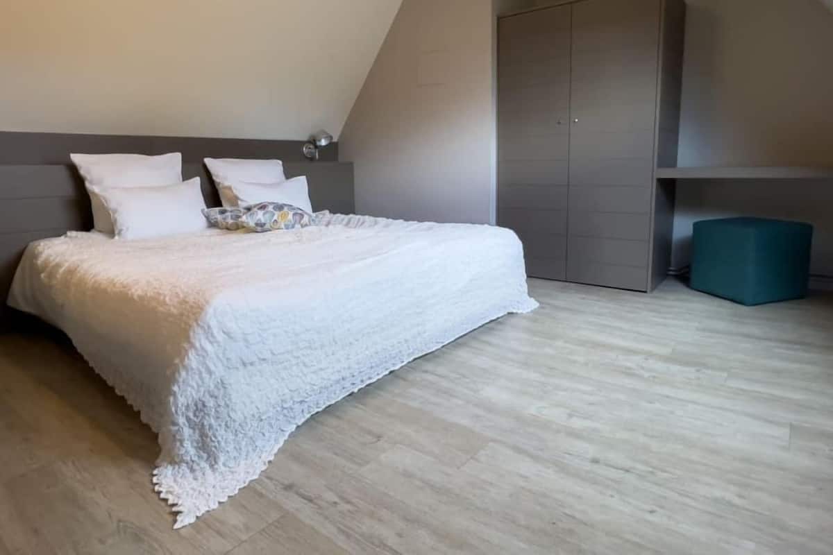 Een slaapkamer met een bed, een kledingkast en een klein, groen poef.