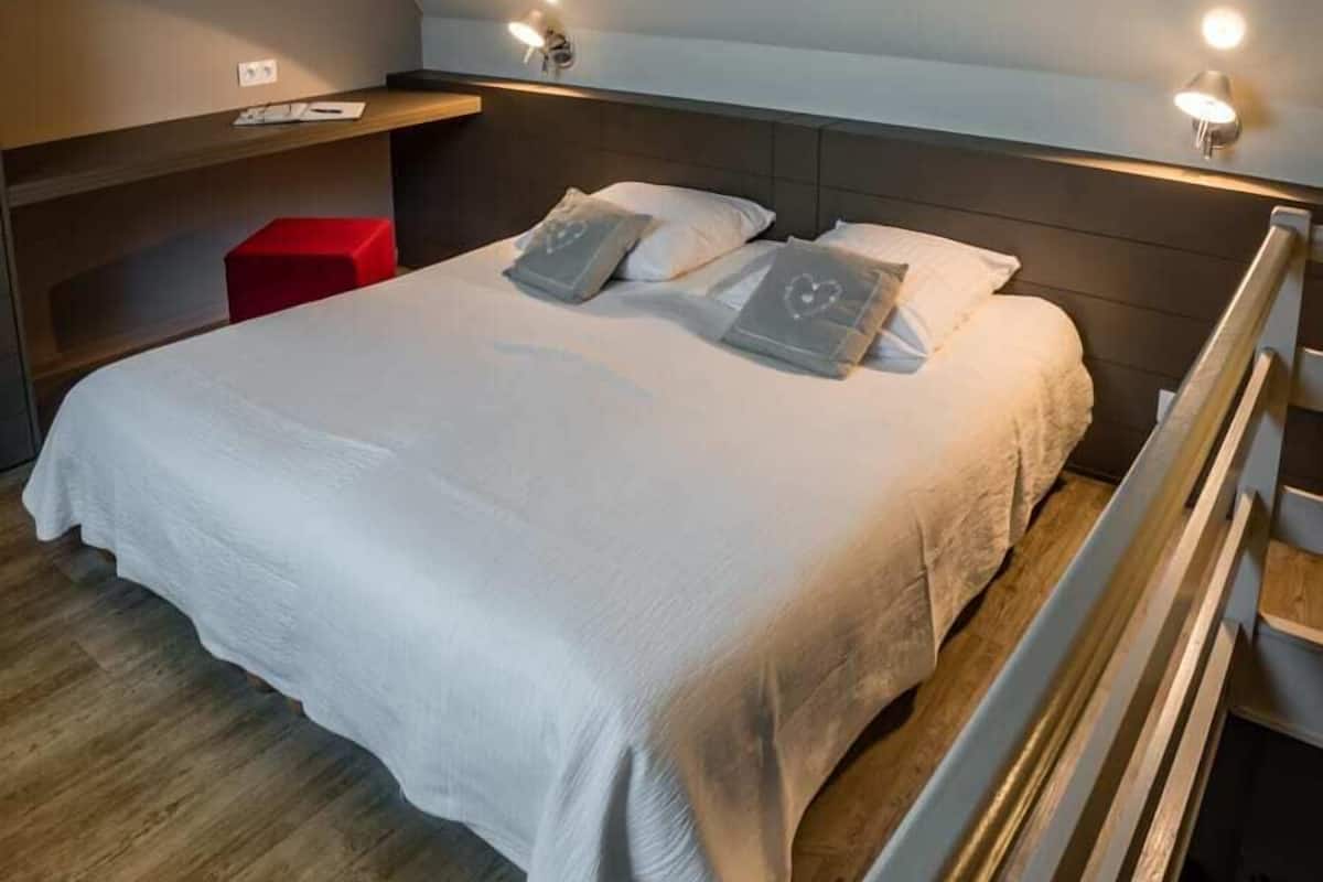 Een slaapkamer met een bed, kussens, een nachtkastje en een rode stoel.
