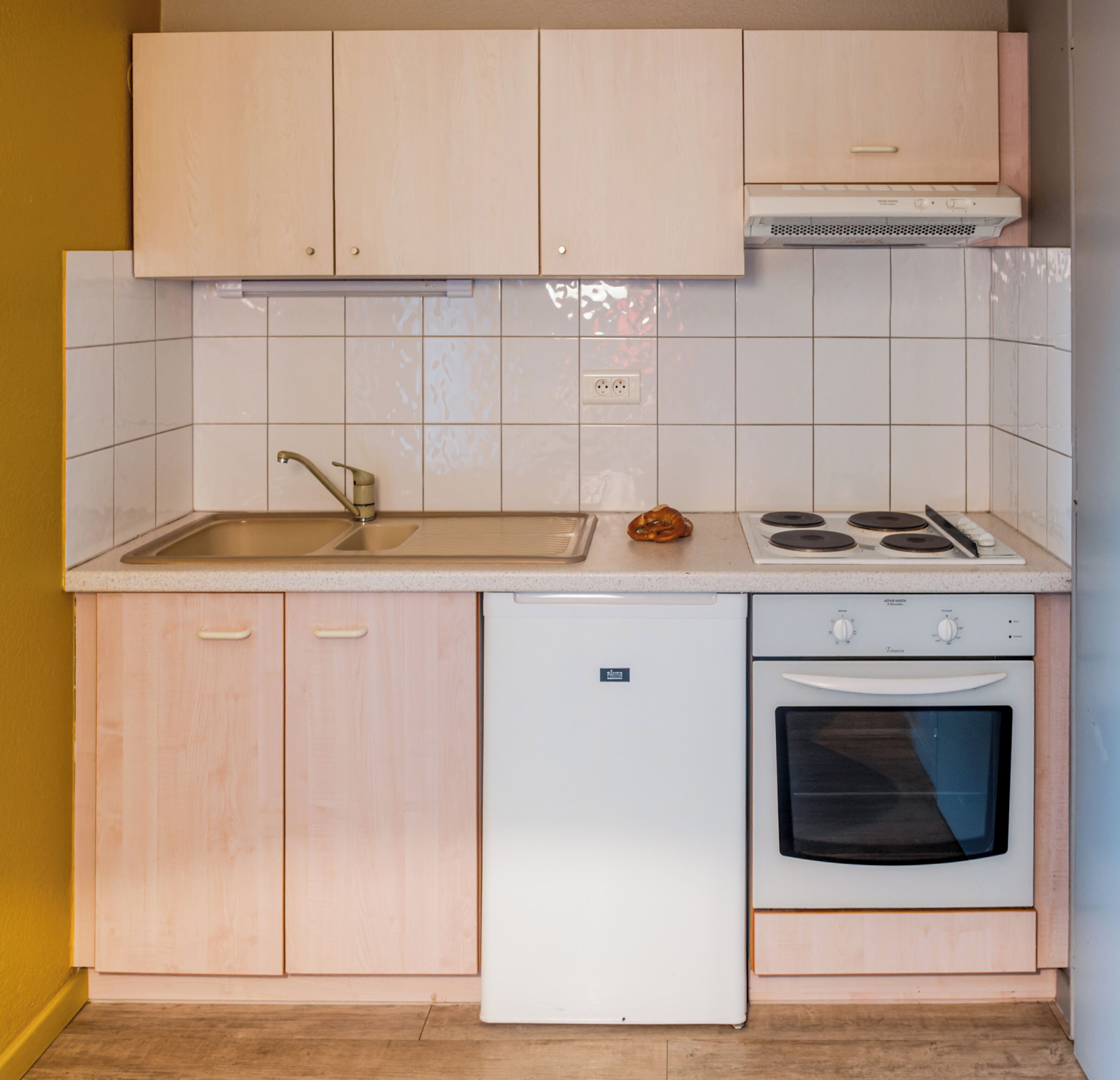 A compact kitchen with light wood cabinets, a white countertop, a built-in dishwasher, a stove, and an oven.