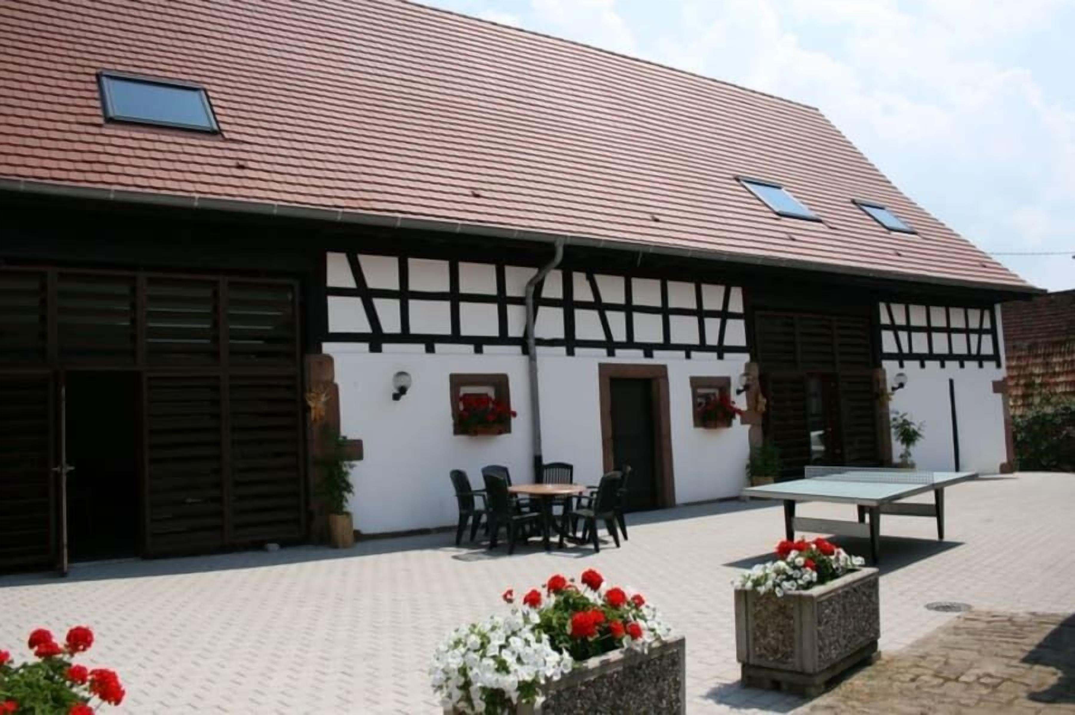 A traditional building with a tiled roof, a courtyard with a table and chairs, and flower planters.