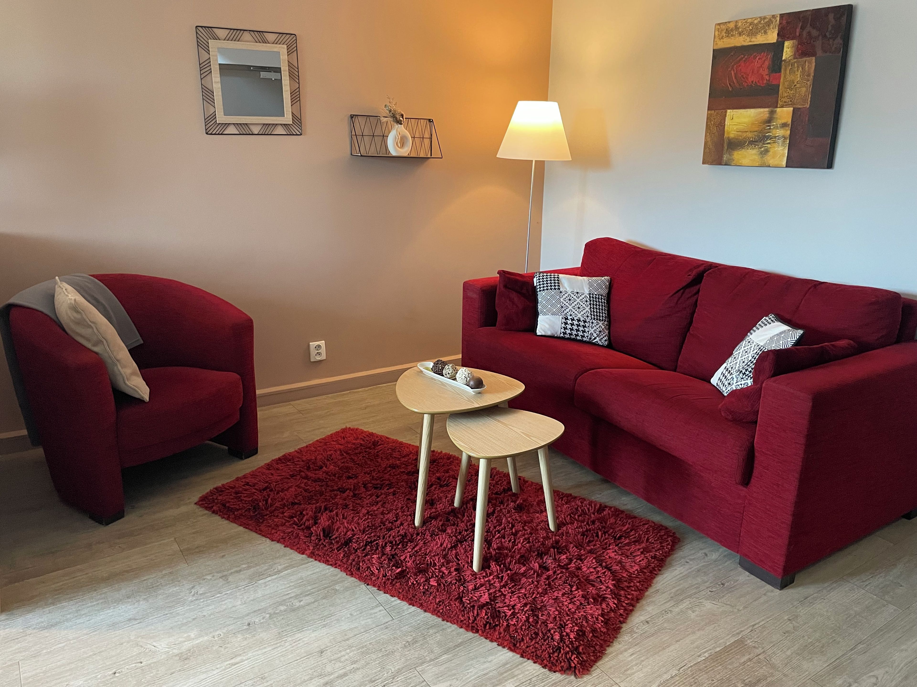 A living room with a red sofa, a red armchair, a small round table, and a red rug.