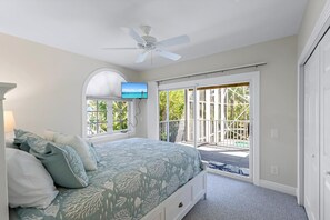 Una camera da letto con un letto, un ventilatore a soffitto, una TV e vista su un balcone con ringhiera.