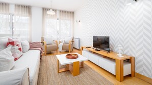 Een moderne woonkamer met een bank, fauteuils, een salontafel, een televisie en een behang met patroon.