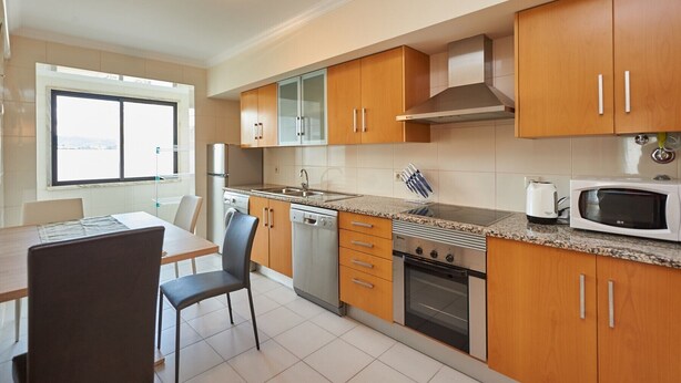 Een moderne keuken met houten kastjes, een granieten aanrecht, een ingebouwde oven, een magnetron en een raam dat natuurlijk licht binnenlaat.