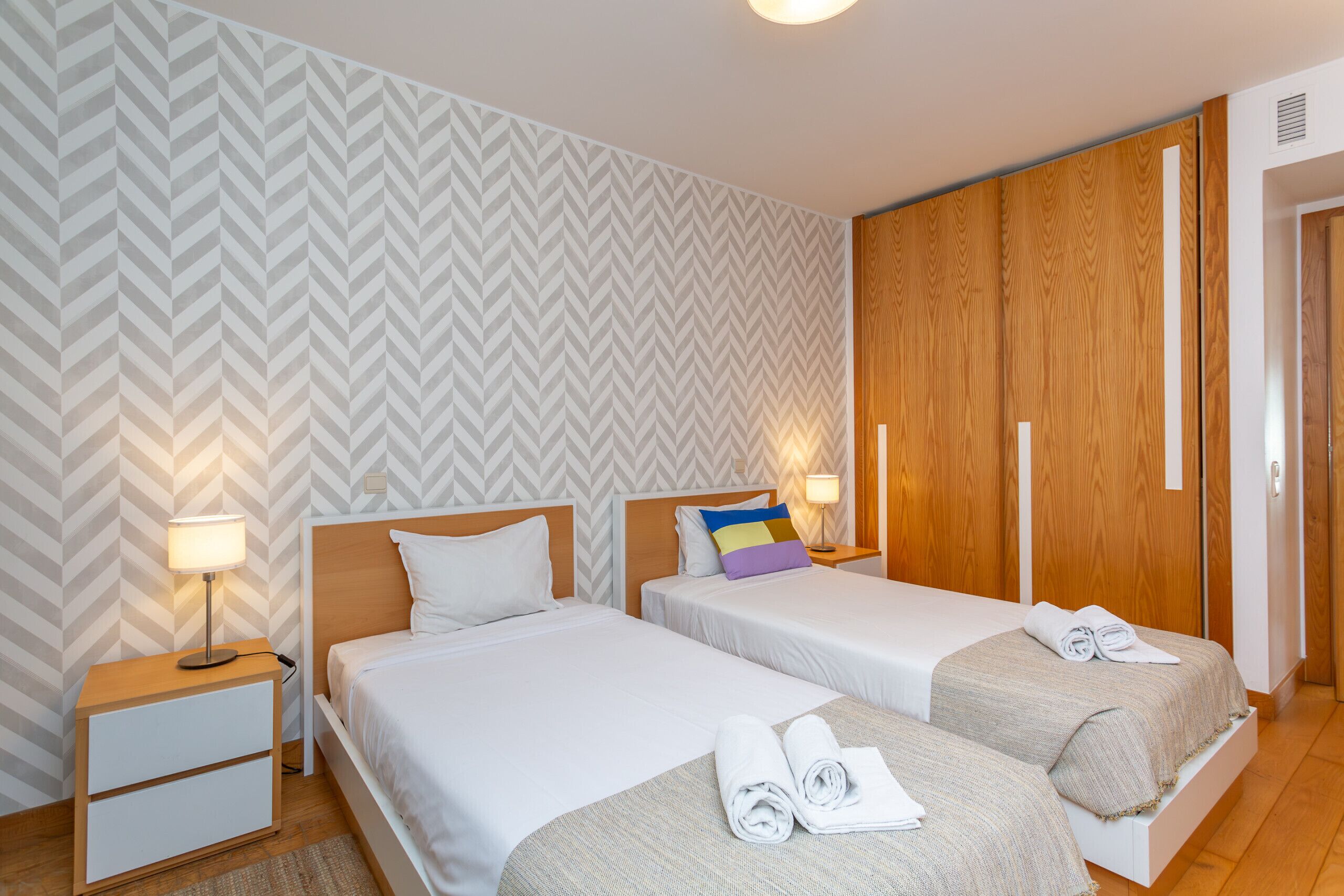 Una habitación de hotel con dos camas, un armario de madera y una mesita de noche con lámpara.